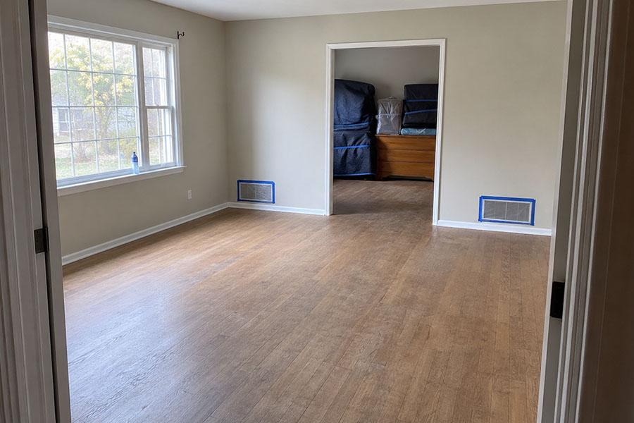 Clean, empty living room fully prepared for professional floor removal, with furniture neatly moved to an adjacent room and HVAC vents sealed